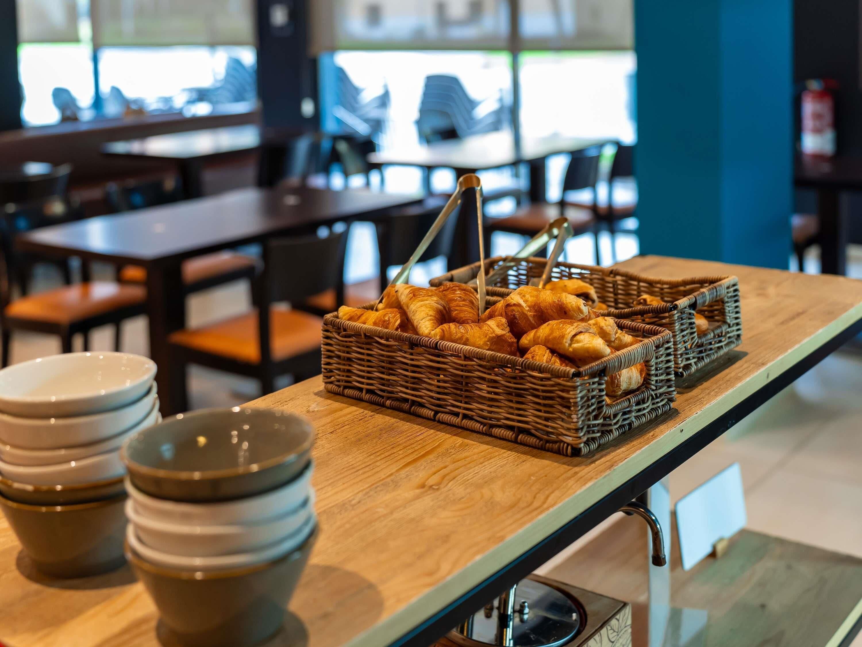 Un interior de restaurante con mesas, sillas, una cesta de mimbre con pasteles y cuencos apilados.