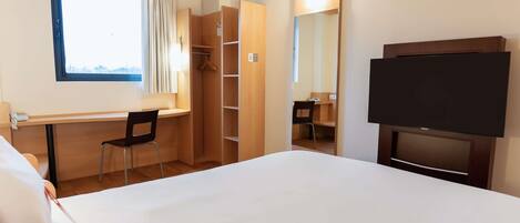 A hotel room with a bed, a desk, a chair, a wardrobe, a mirror, and a TV.