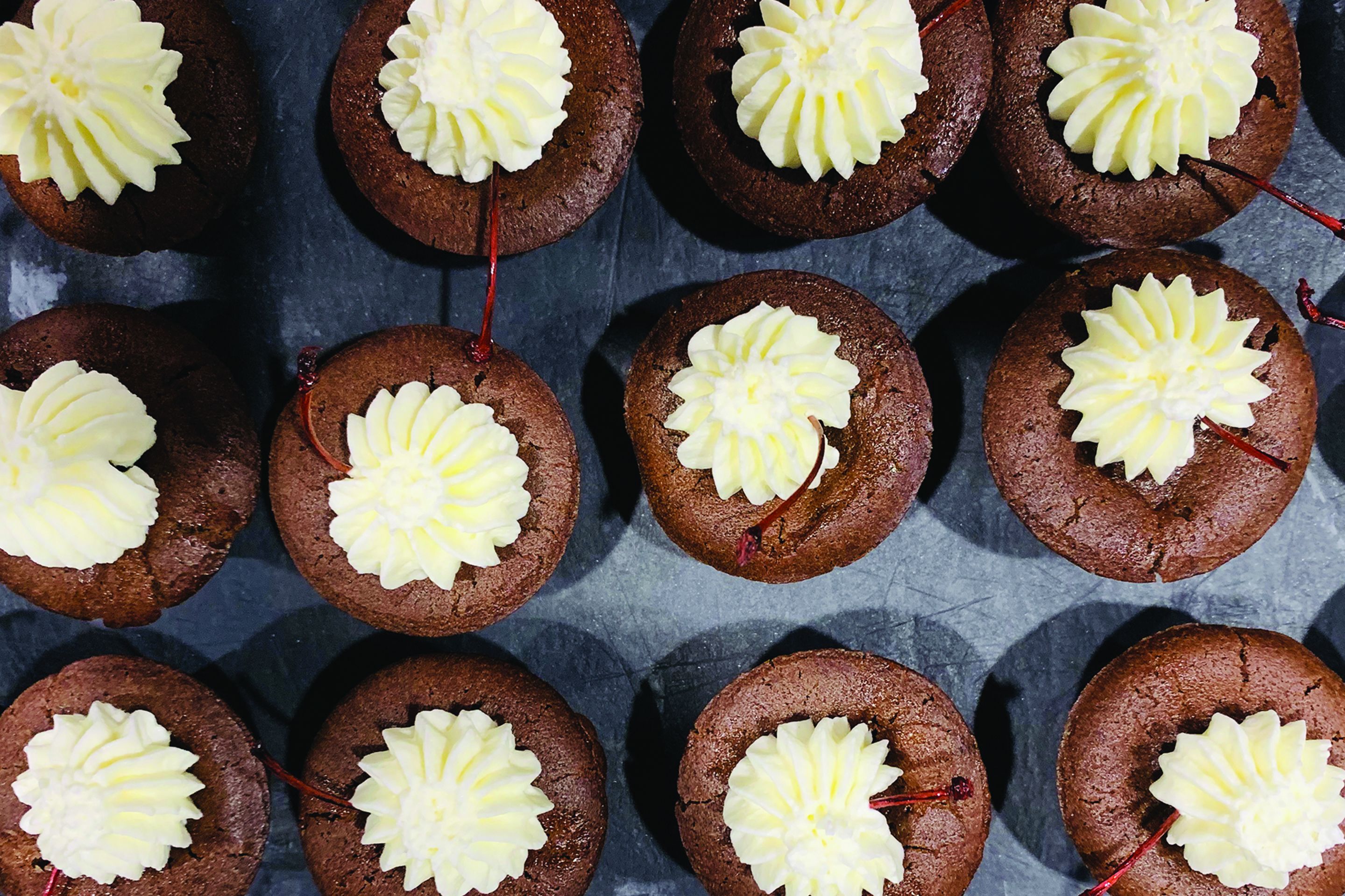 Una composizione di cupcakes al cioccolato con glassa bianca su una superficie scura.