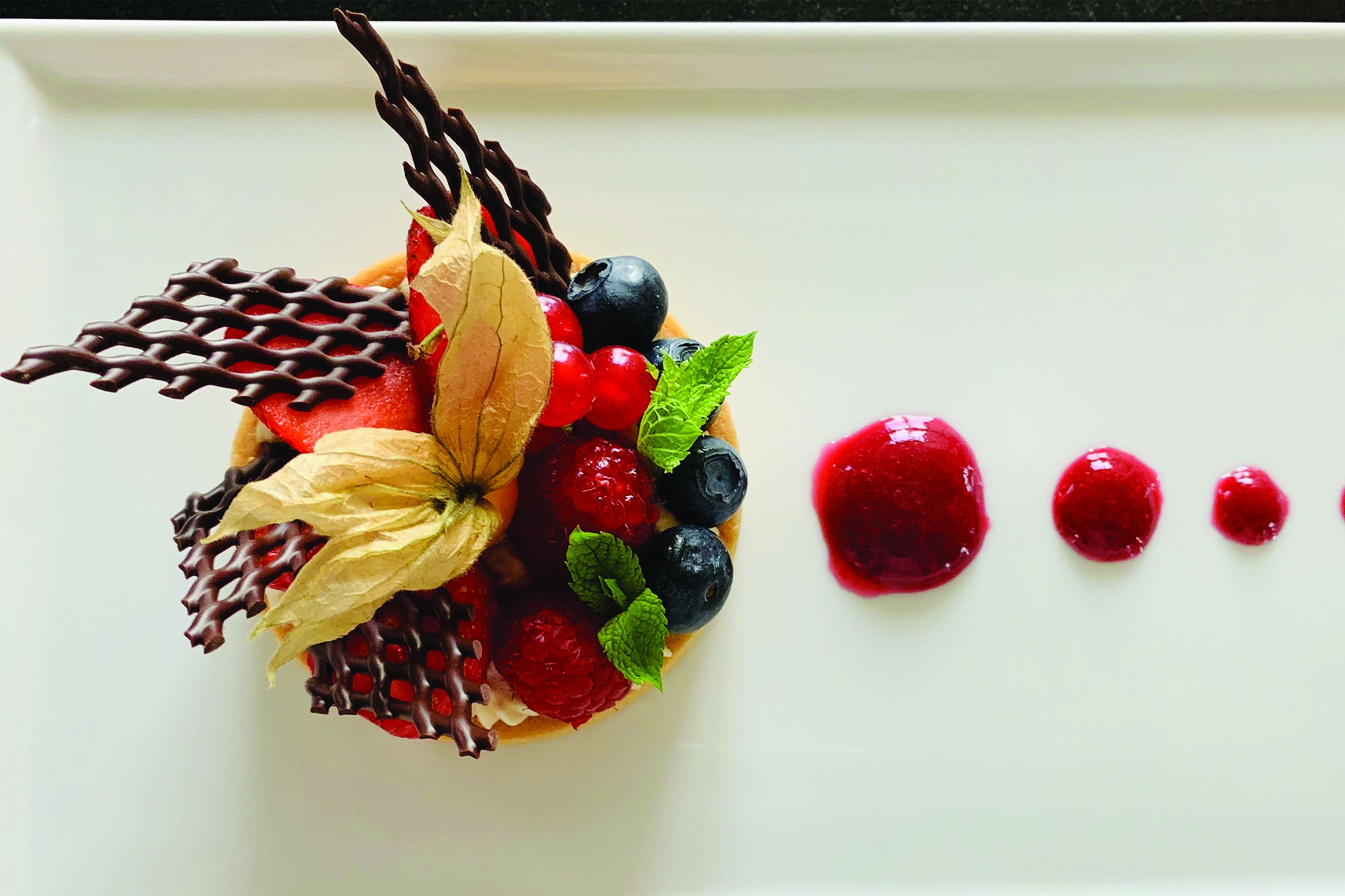 A dessert with strawberries, blueberries, and chocolate on a white plate.