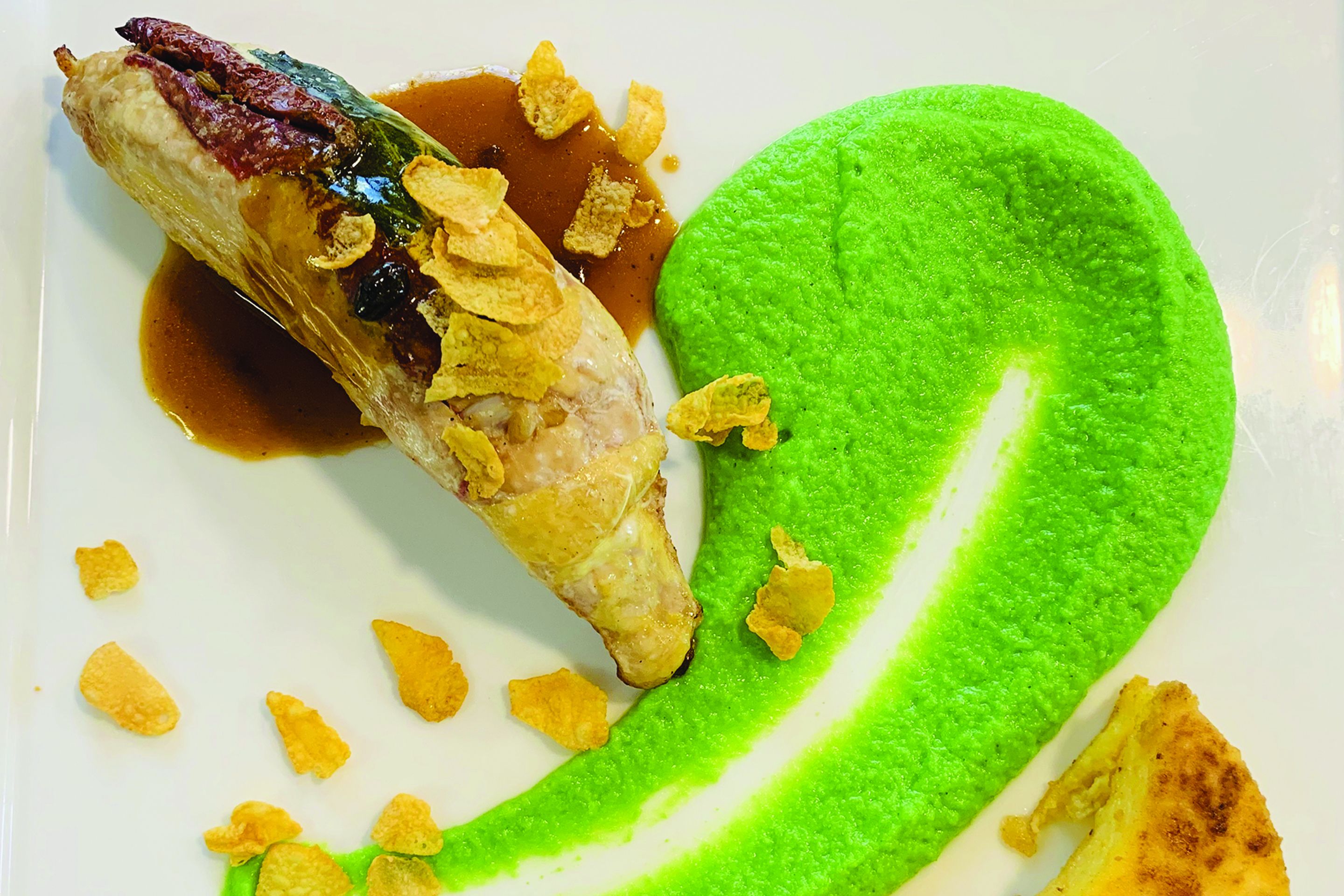Un plato blanco con un puré verde y un relleno, posiblemente un pimiento relleno.