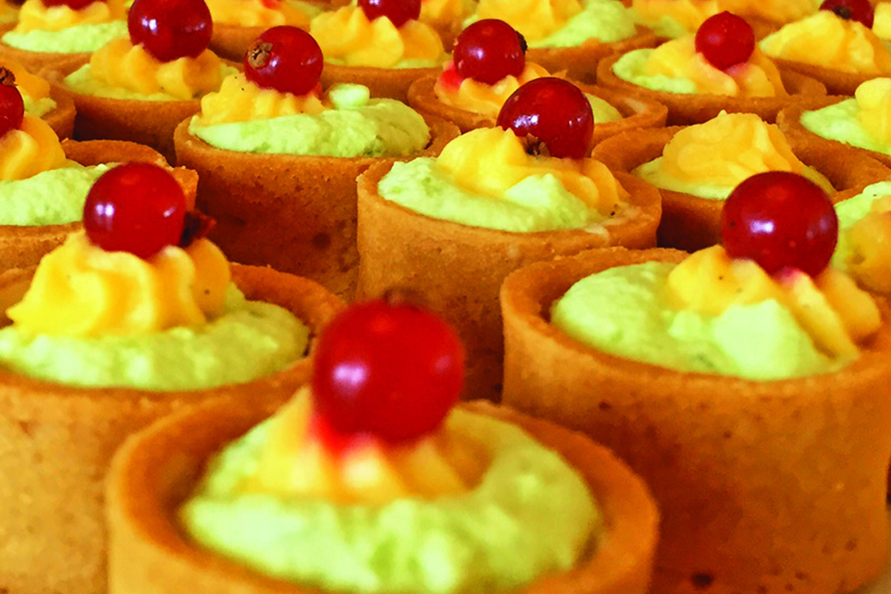 Gros plan sur de petites tartes garnies d’une crème onctueuse et surmontées d’une cerise.
