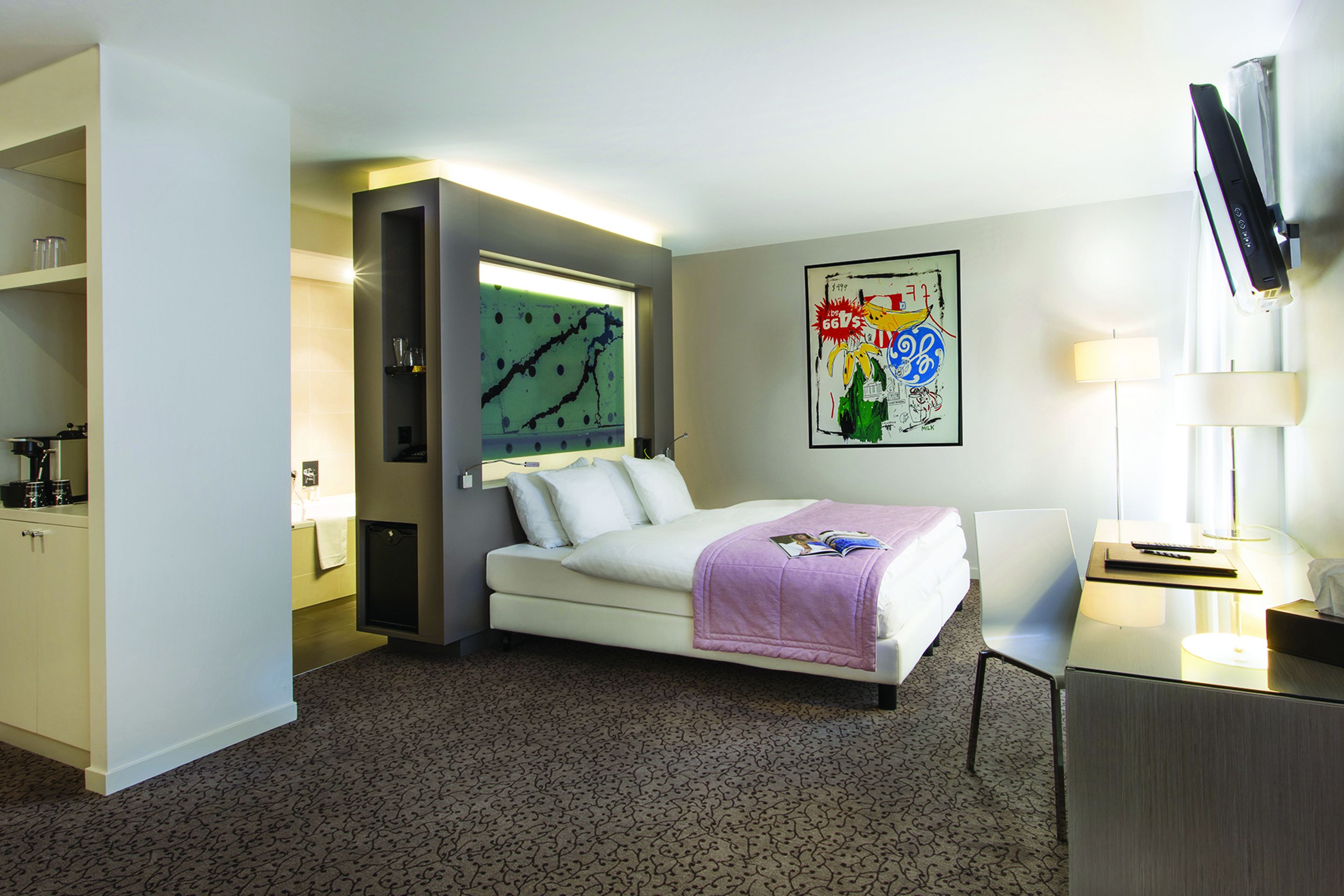 Ein Hotelzimmer mit Bett, Schreibtisch, Stuhl, Fernseher und einem Gemälde an der Wand.