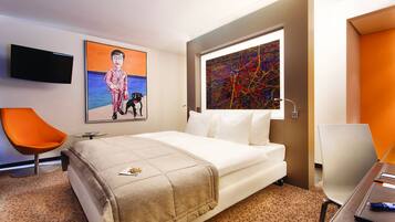 Une chambre d’hôtel avec un lit, une télévision, un tableau et un bureau avec une chaise.