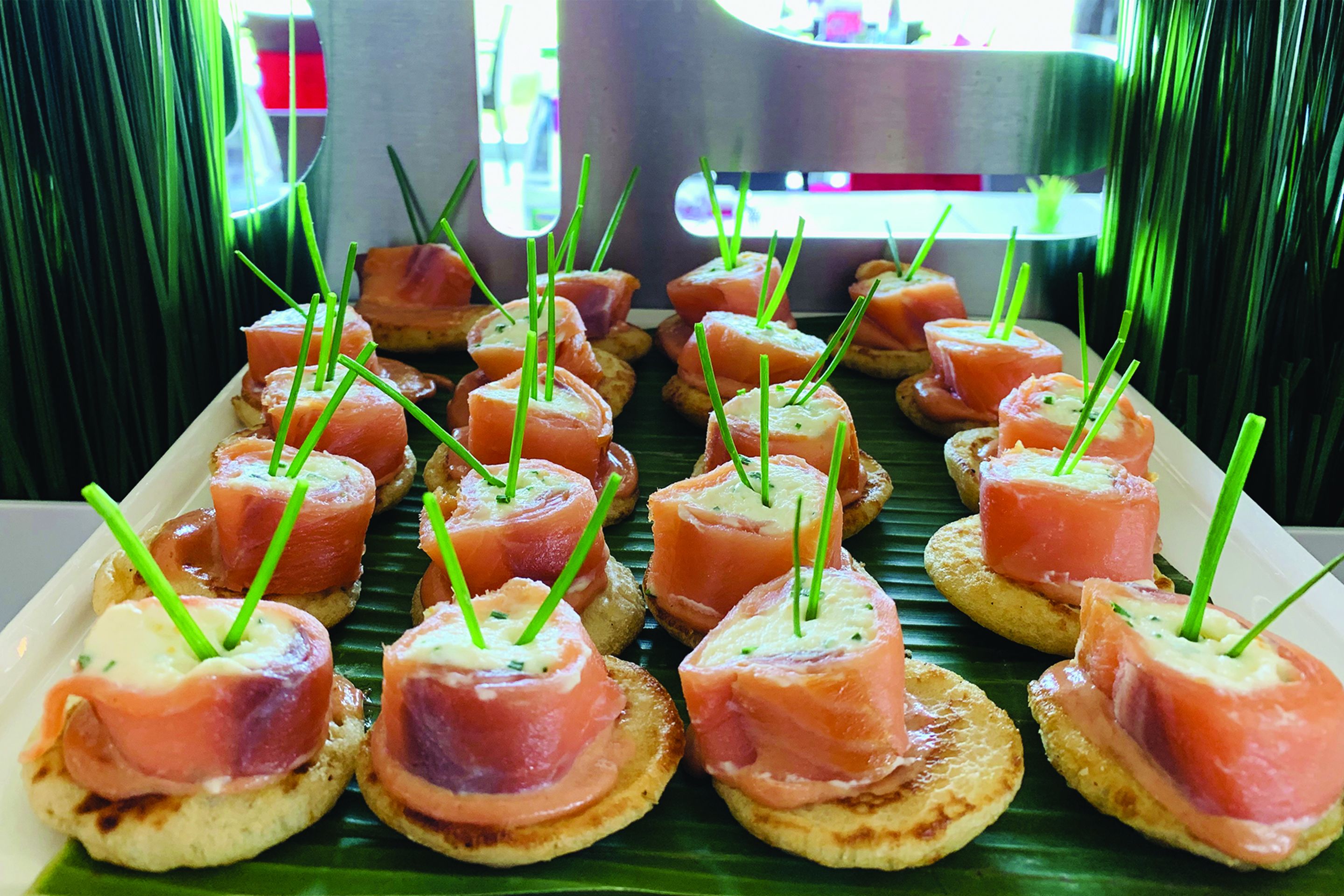Een schaal met hapjes, gerookte zalm en groene bieslook op kleine broodjes.