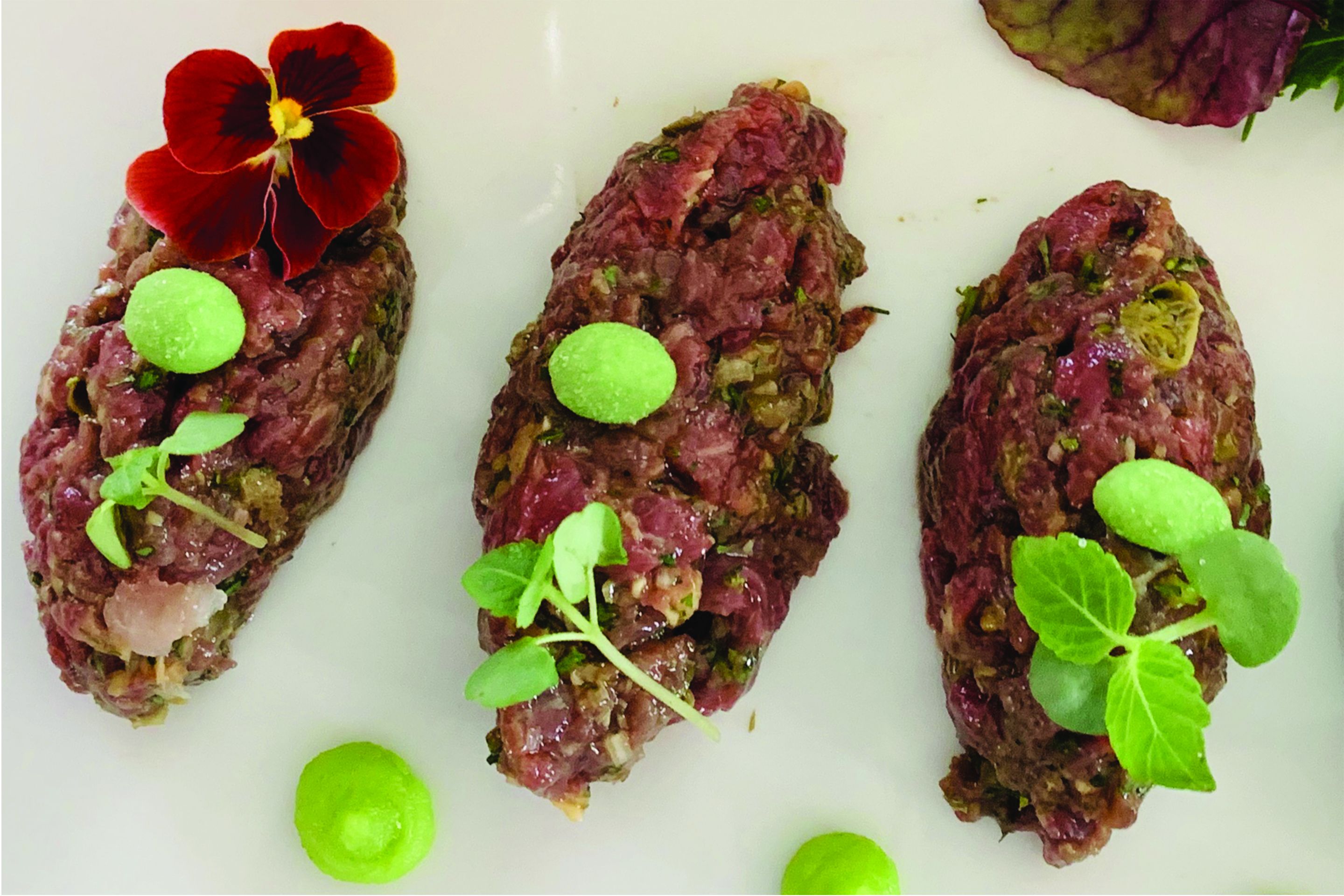 A plate with three meat-based dishes, each garnished with green leaves and a red flower.
