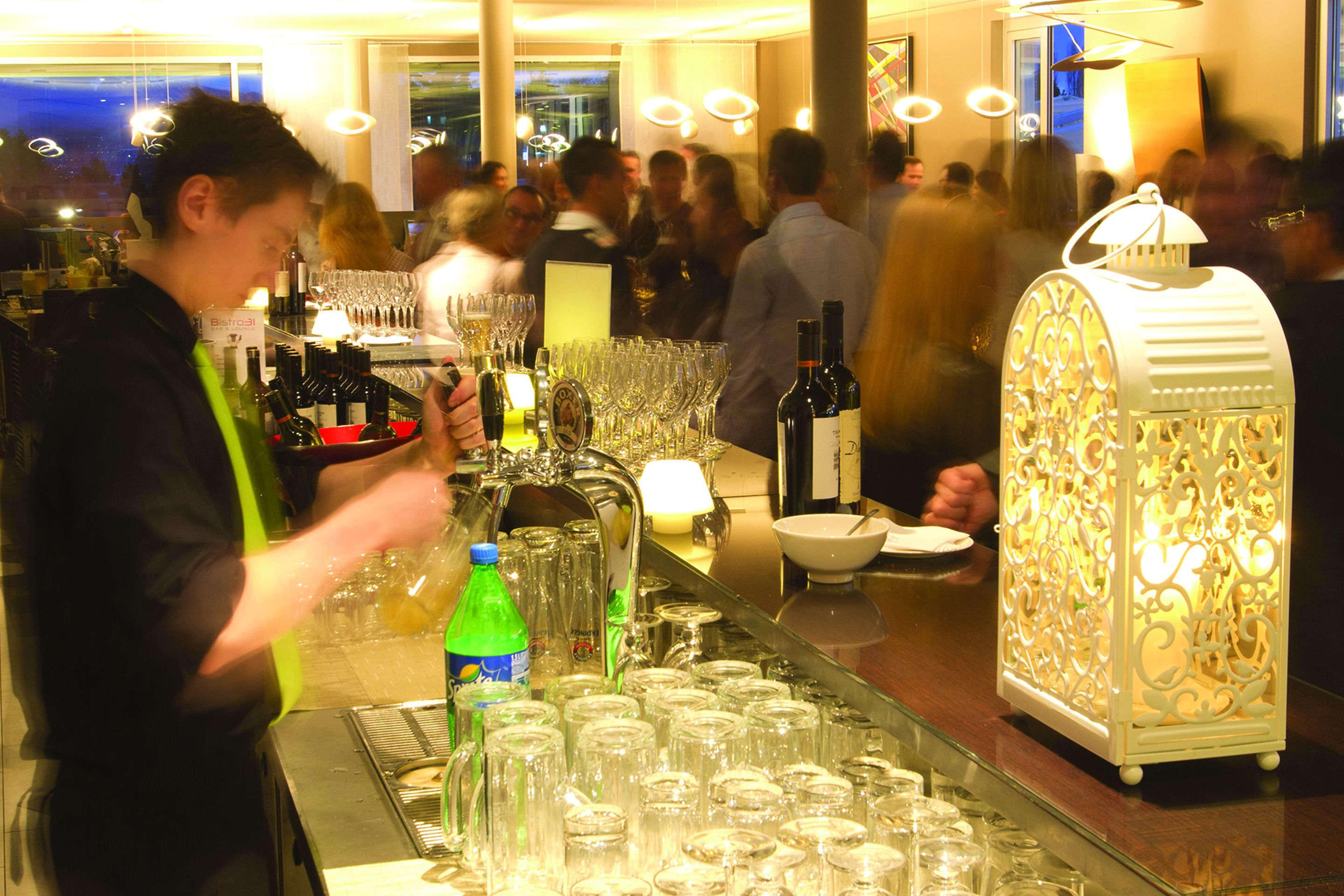 A bar area with a bartender preparing drinks, a well-stocked bar with bottles and glasses, and a decorative lantern.