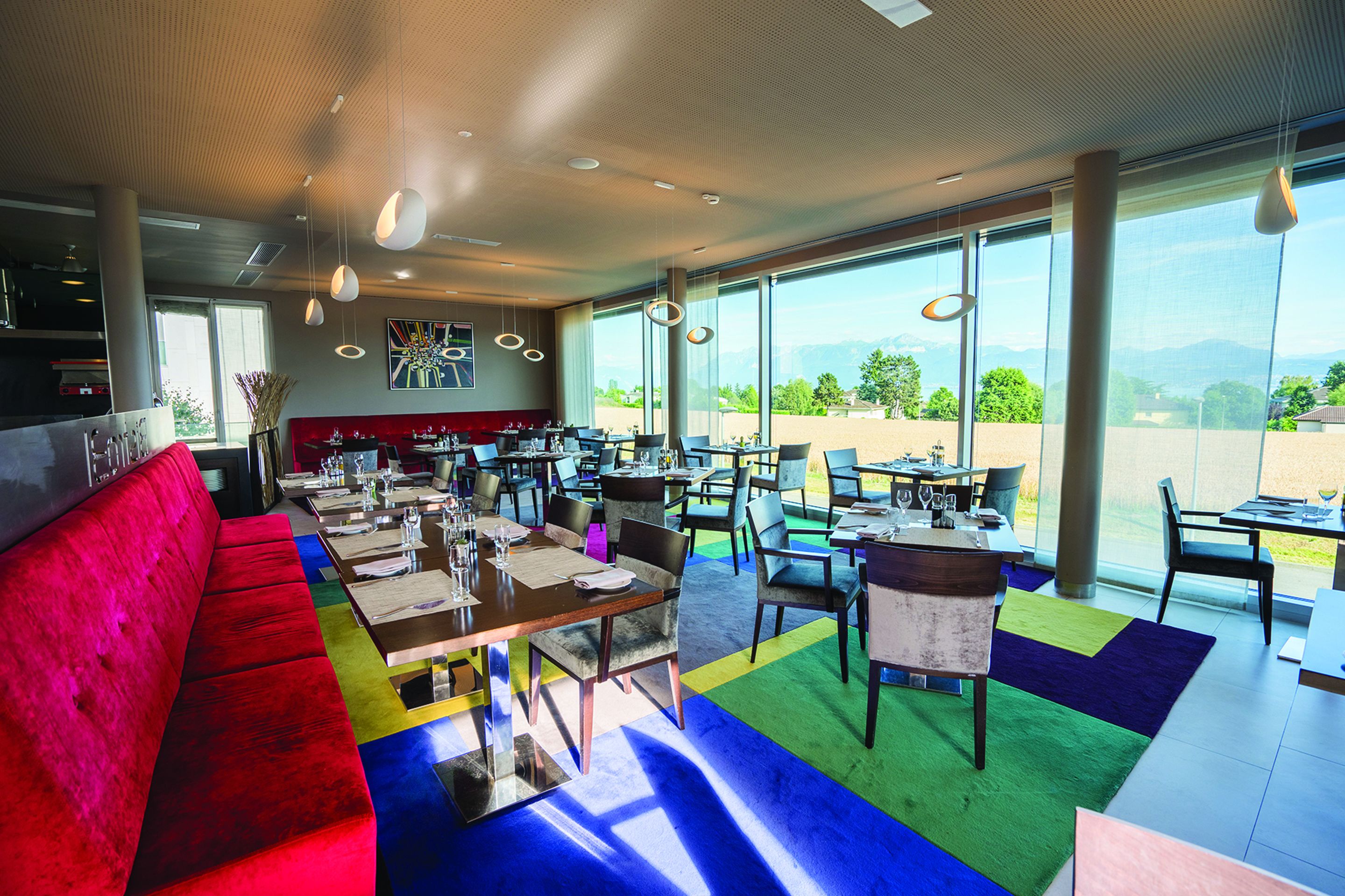 Un restaurante moderno con una zona de estar roja, varias mesas y ventanas amplias que ofrecen vistas al exterior.