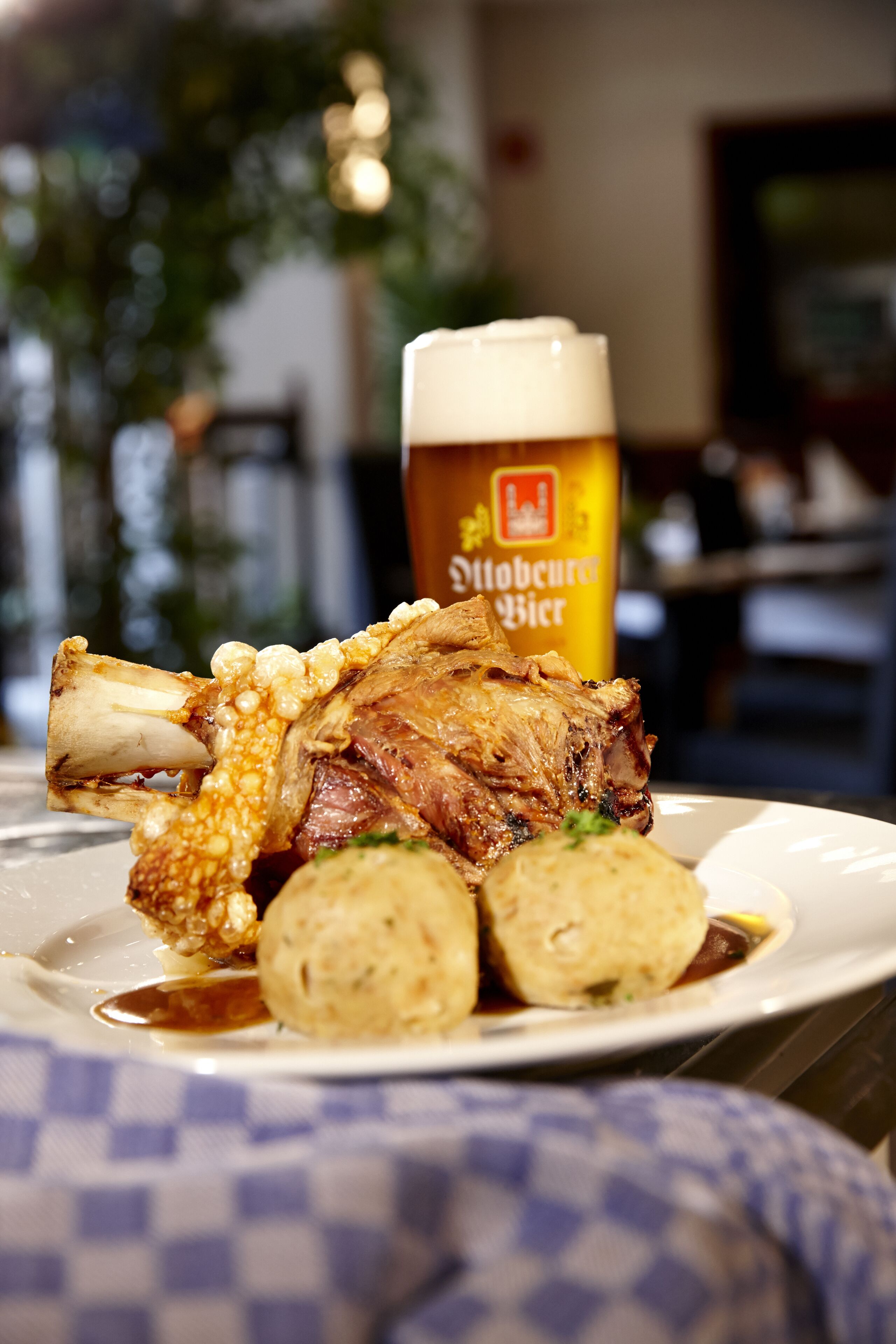 A plate with a roasted lamb shank, a rolled potato, and a glass of beer.