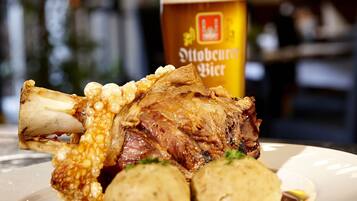 A plate with a roasted lamb shank, a rolled potato, and a glass of beer.