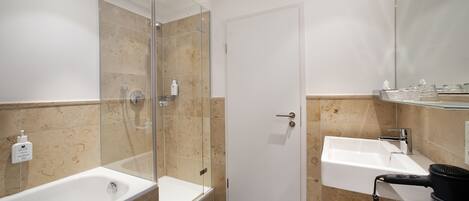 Un baño moderno con ducha envuelta en vidrio, bañera independiente y lavamanos con secador de pelo.