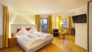 Ein Hotelzimmer mit zwei Betten, Holzboden, einem Schreibtisch mit Stuhl, einem Fernseher und Blick auf Gebäude durch das Fenster.