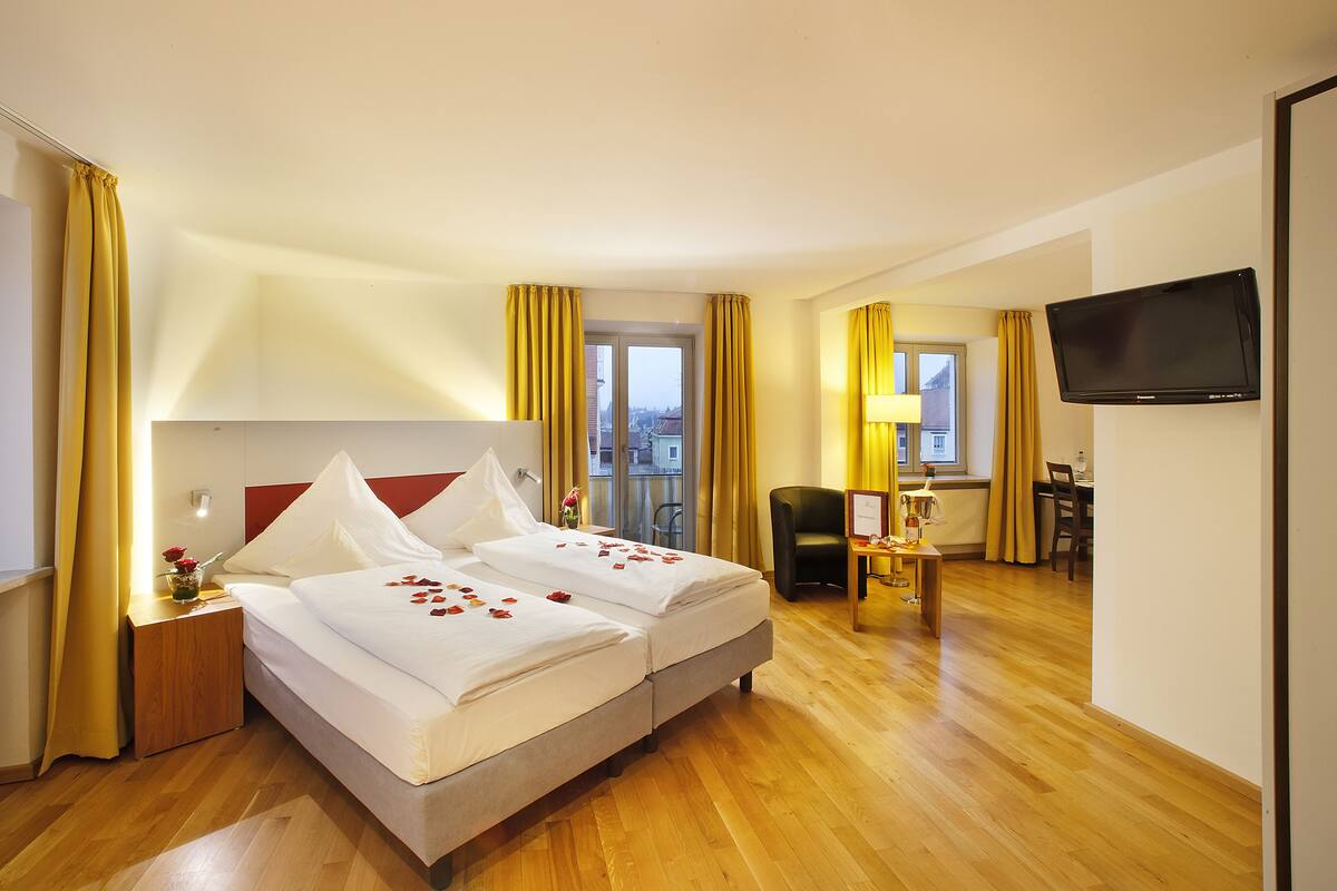 Une chambre d’hôtel avec deux lits, un plancher en bois, un bureau avec une chaise, une télévision et une vue sur les bâtiments par la fenêtre.