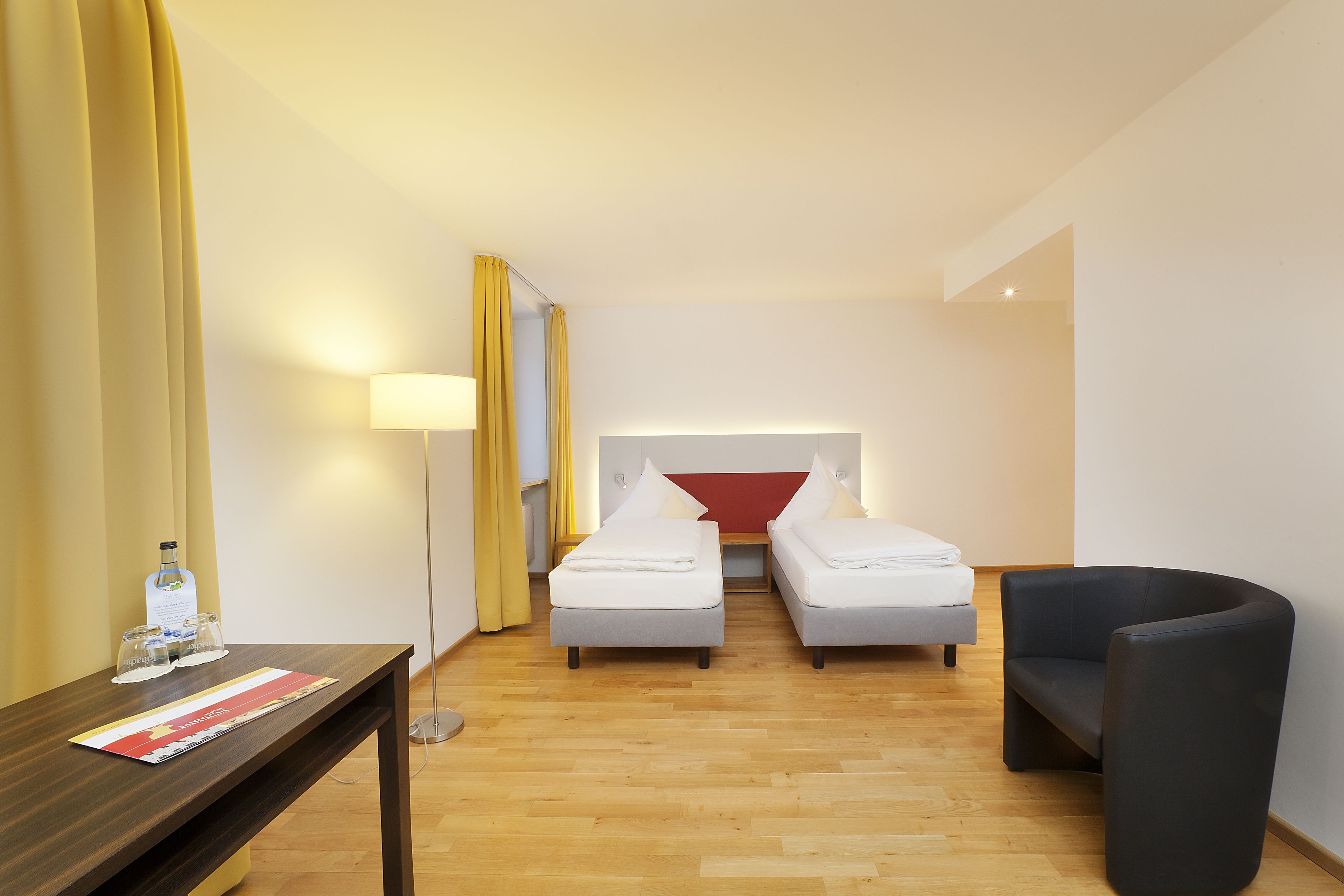 A hotel room with two single beds, a desk with a lamp, a chair, and a bottle of water on the desk.