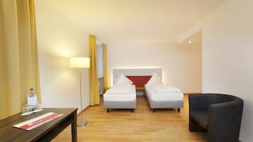 A hotel room with two single beds, a desk with a lamp, a chair, and a bottle of water on the desk.