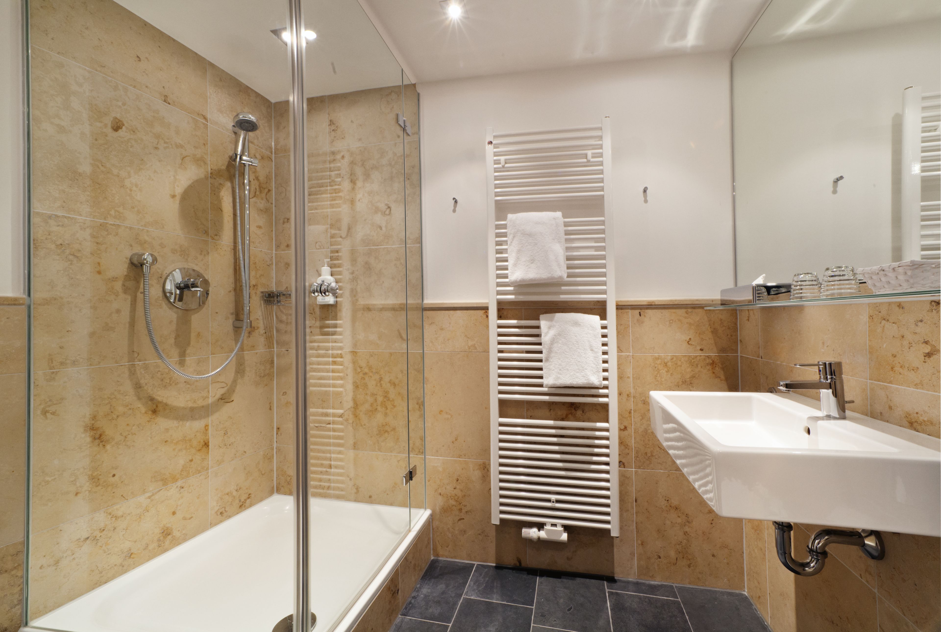 A modern bathroom with a glass-enclosed shower, a white bathtub, a built-in sink, and a towel rack with multiple towels.