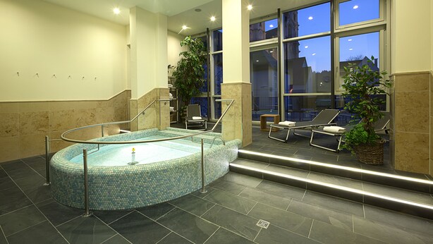 Ein Wellnessbereich mit Whirlpool, Liegestühlen und großen Fenstern.