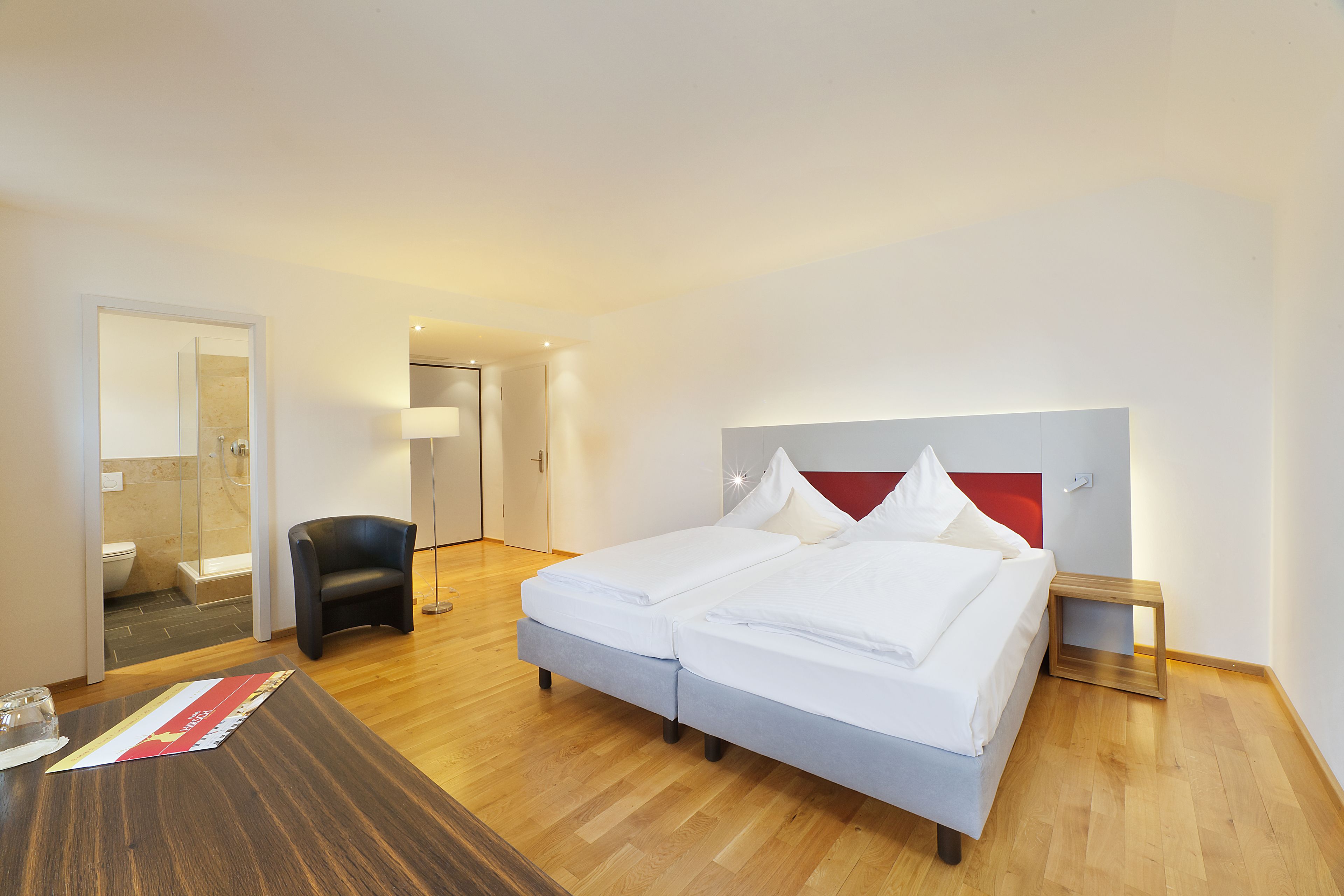 Habitación de hotel con cama doble, mesita de noche, una silla, suelo de madera y un espejo.