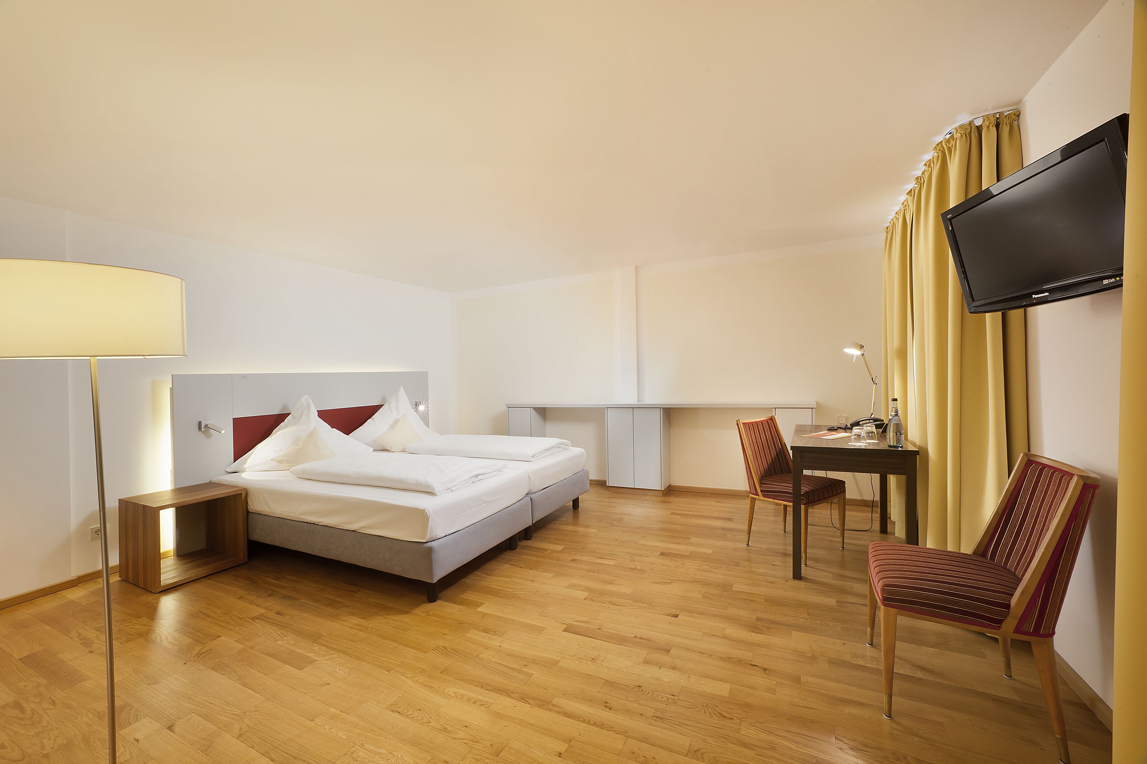 Una habitación de hotel con cama, escritorio, silla, televisor y lámpara.