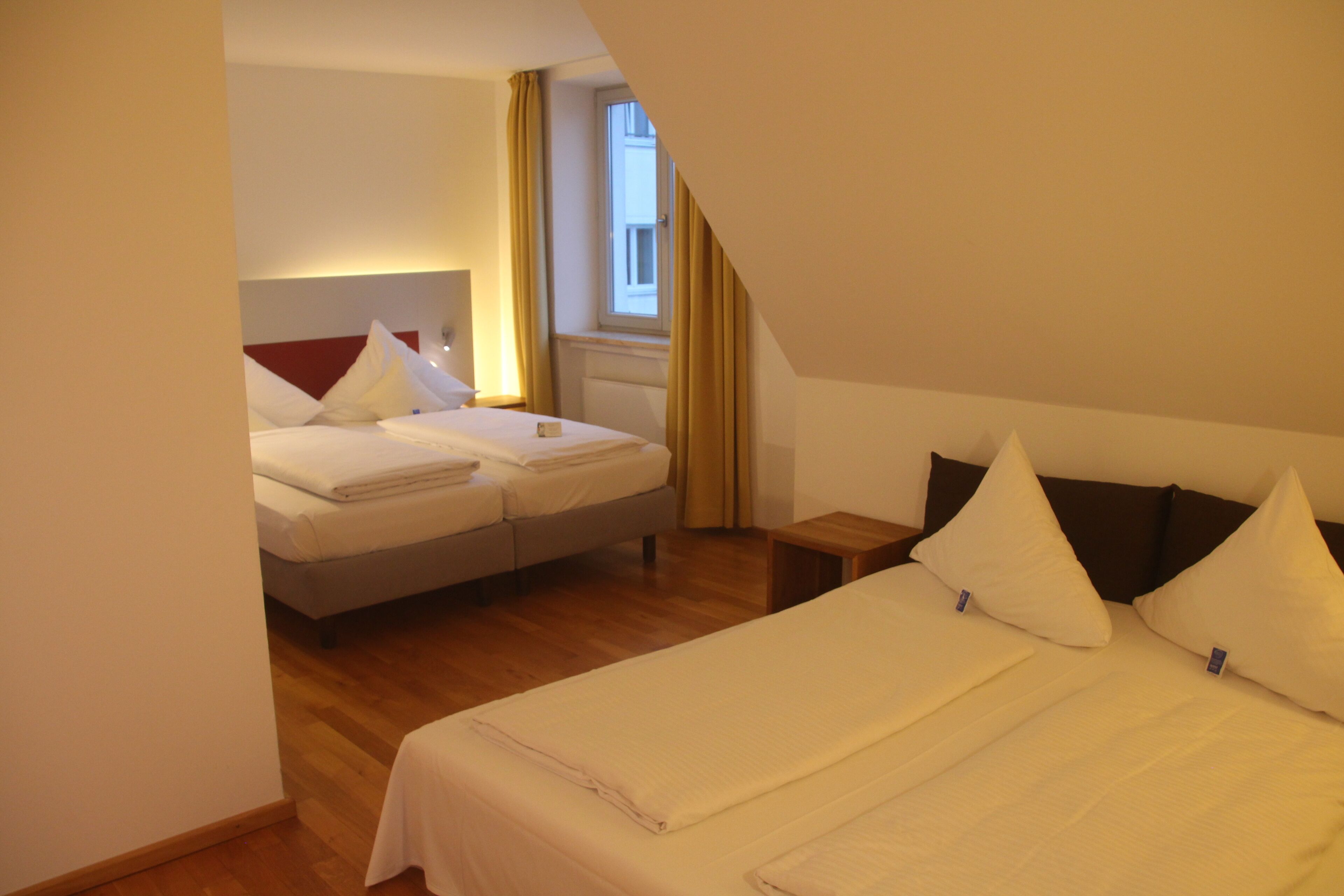 A hotel room with two beds, a window with curtains, and a wooden floor.