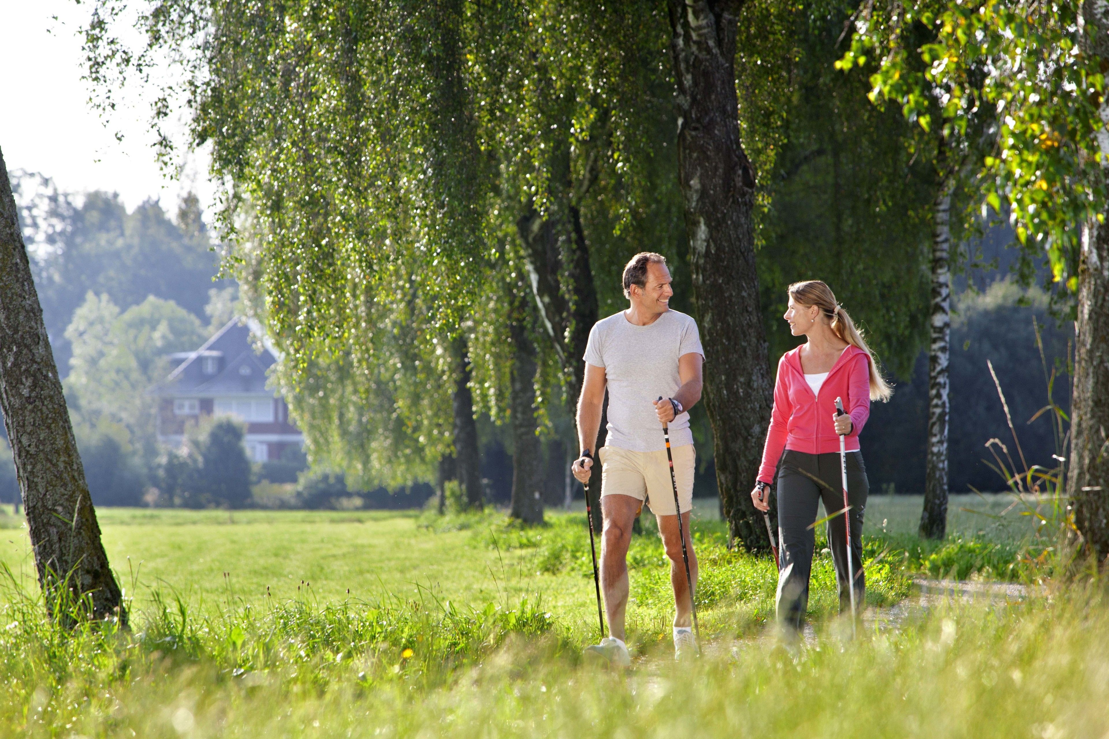 Two people walking in a grassy park area with trees and a house in the background.