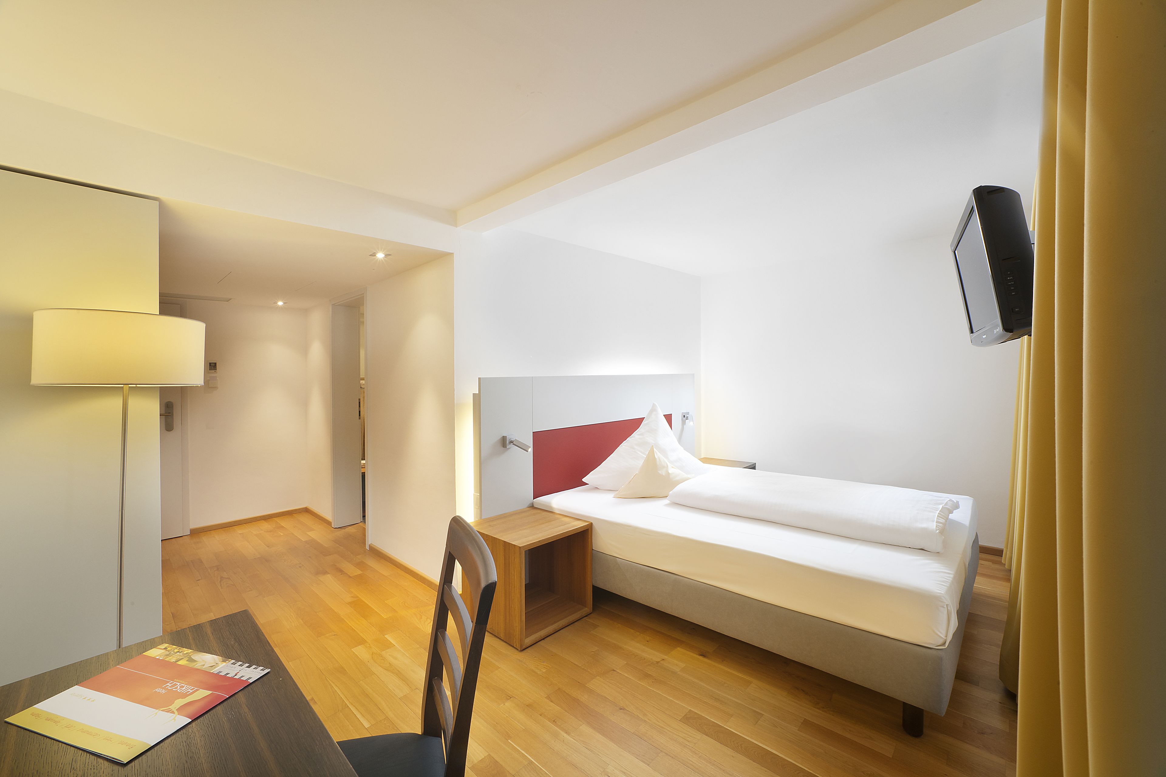 A compact hotel room with a single bed, a desk, and a chair.