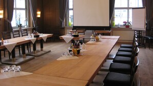 Ein Konferenzraum mit langen Tischen, Stühlen und einer großen Leinwand.