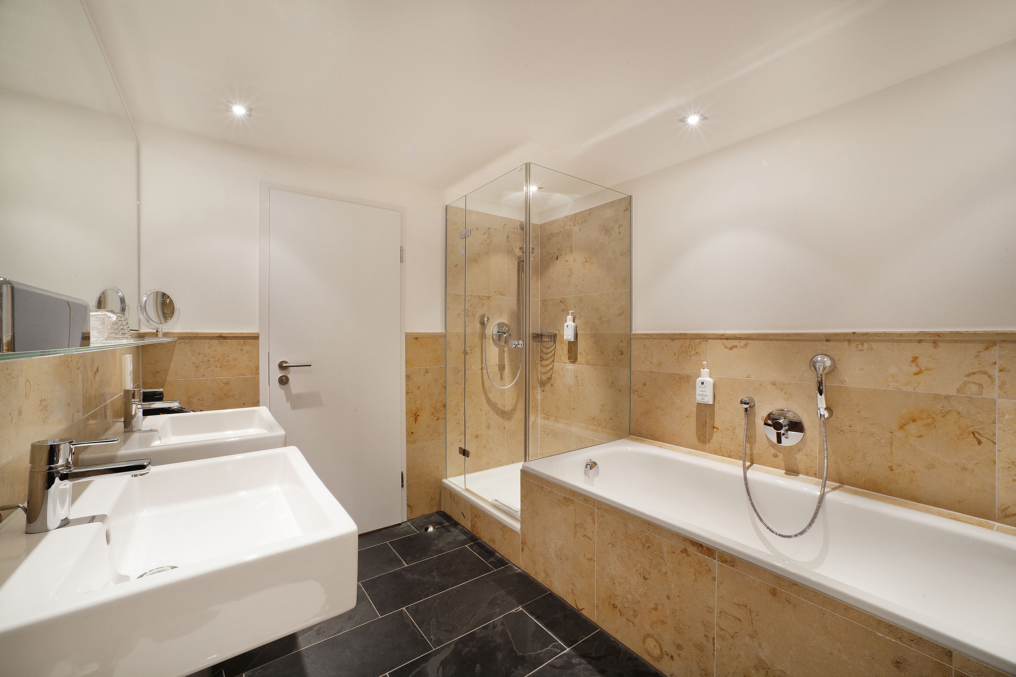 Un baño moderno con dos lavamanos, ducha con cerramiento de vidrio y una bañera grande.