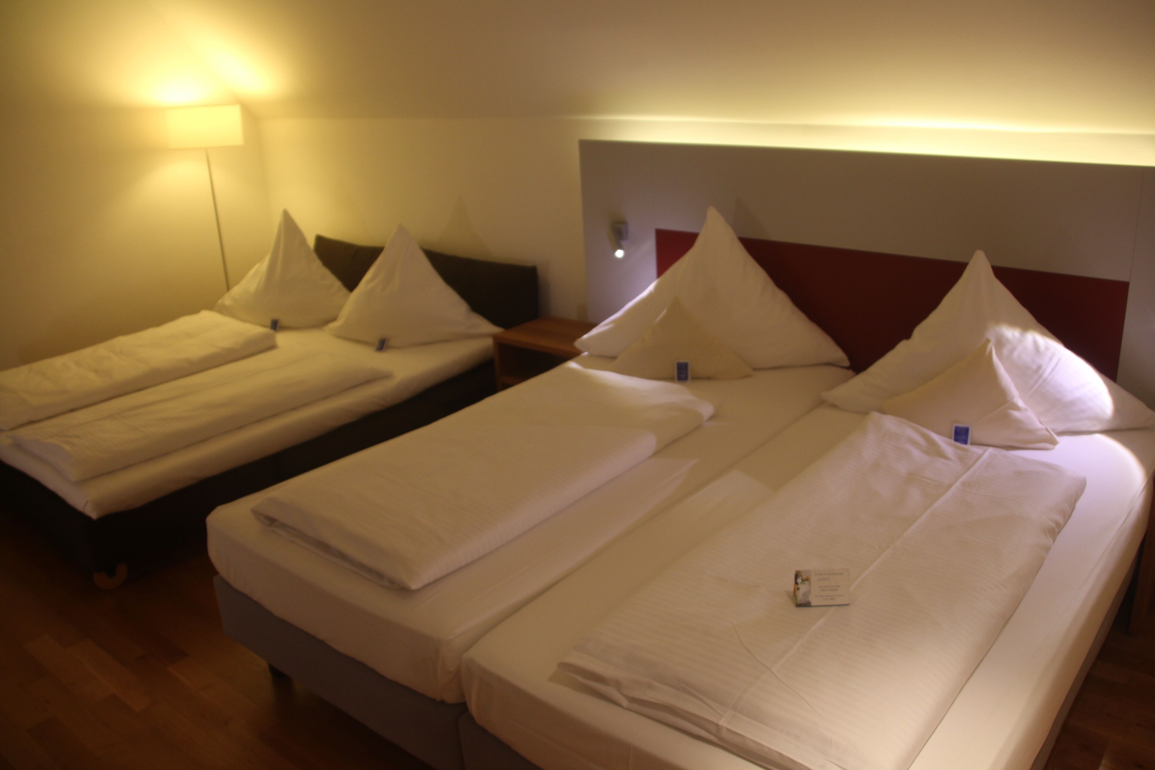 A hotel room with three single beds arranged in a row, each with white bedding and pillows.
