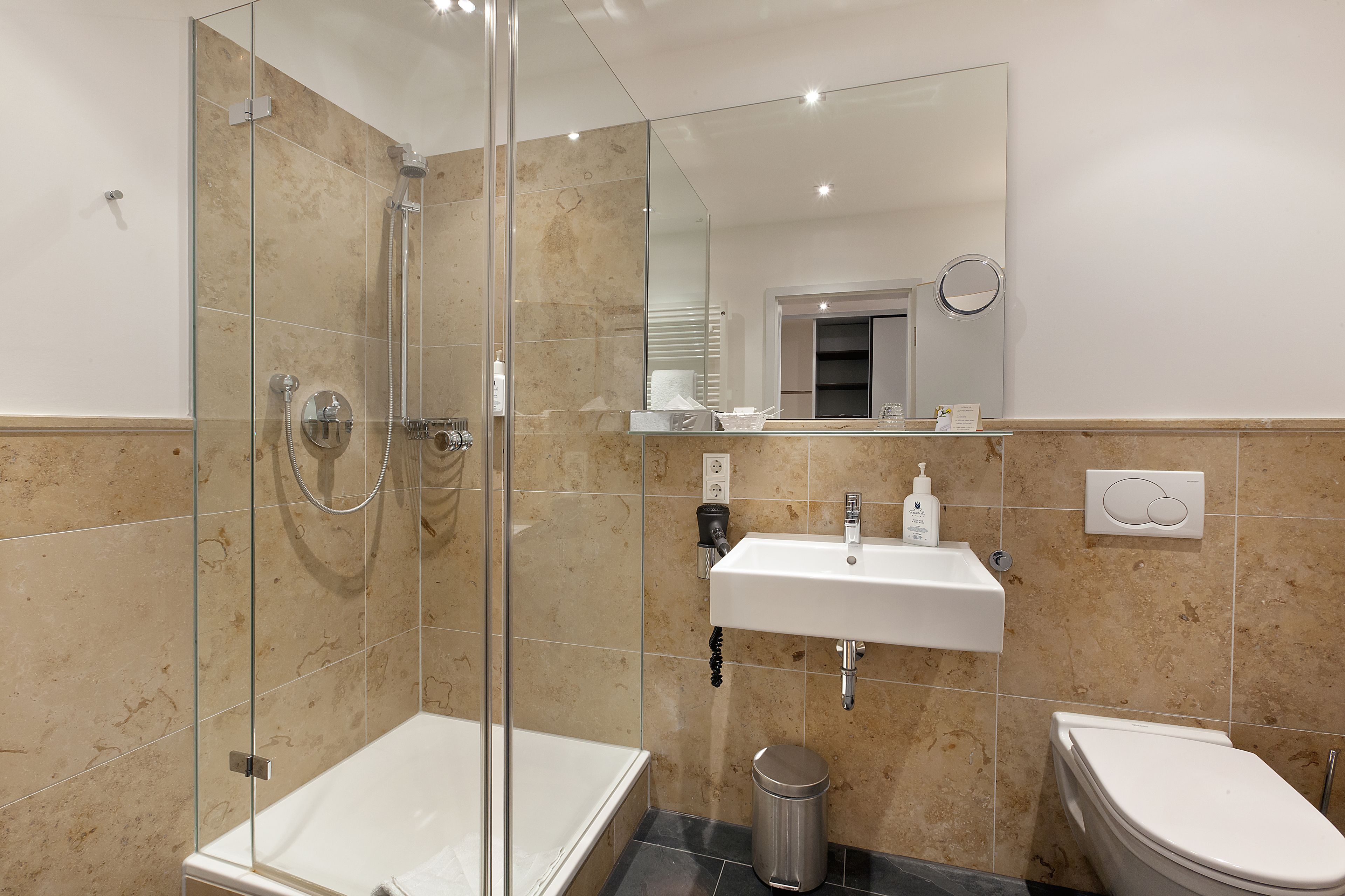 Un baño moderno con ducha envuelta en vidrio, un lavamanos blanco y un inodoro.