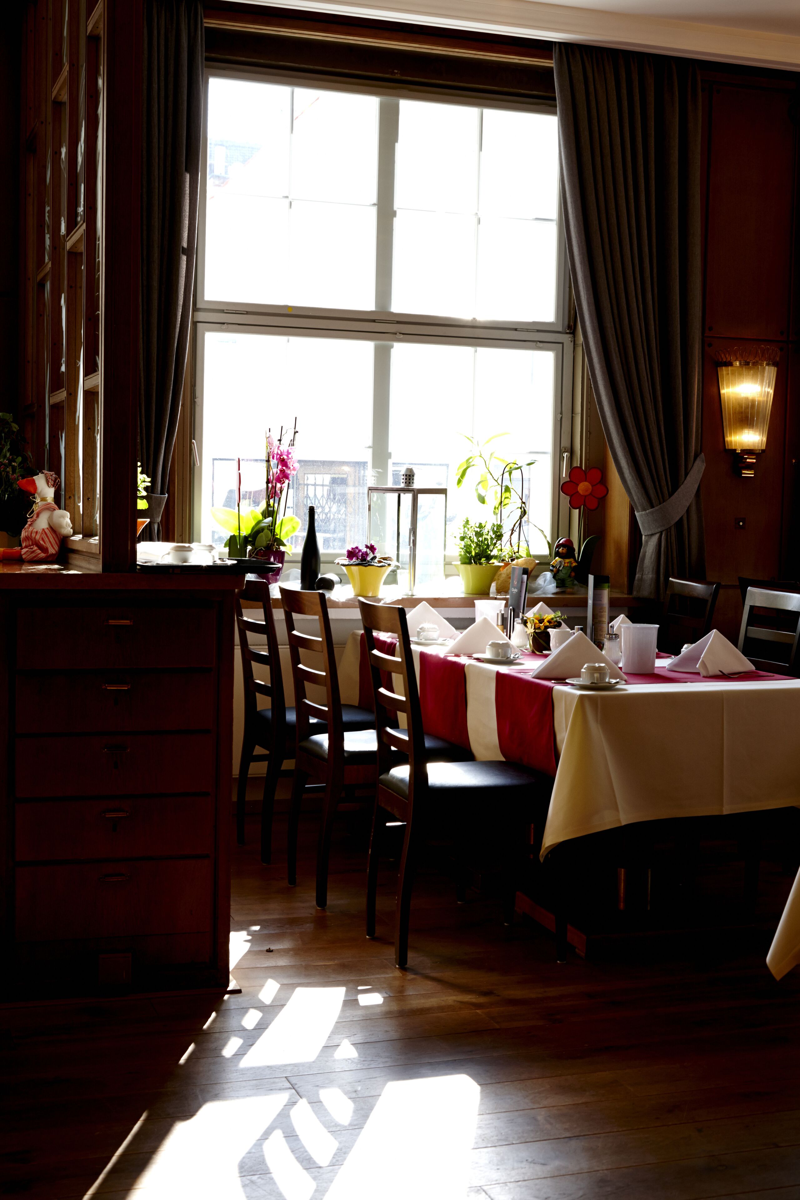 Un comedor con una mesa dispuesta para dos, una ventana con cortinas y piso de madera.