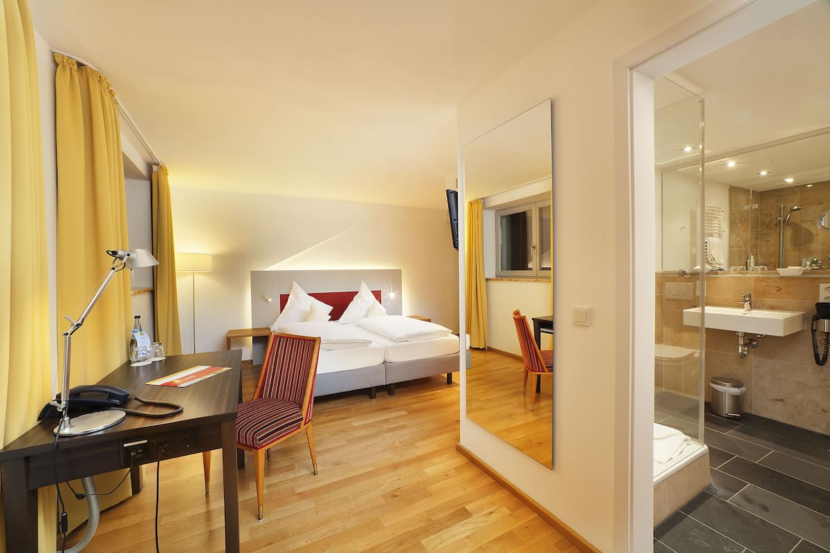 Une chambre d’hôtel comprenant un lit, un bureau, une chaise et une salle de bain avec un lavabo et un miroir.