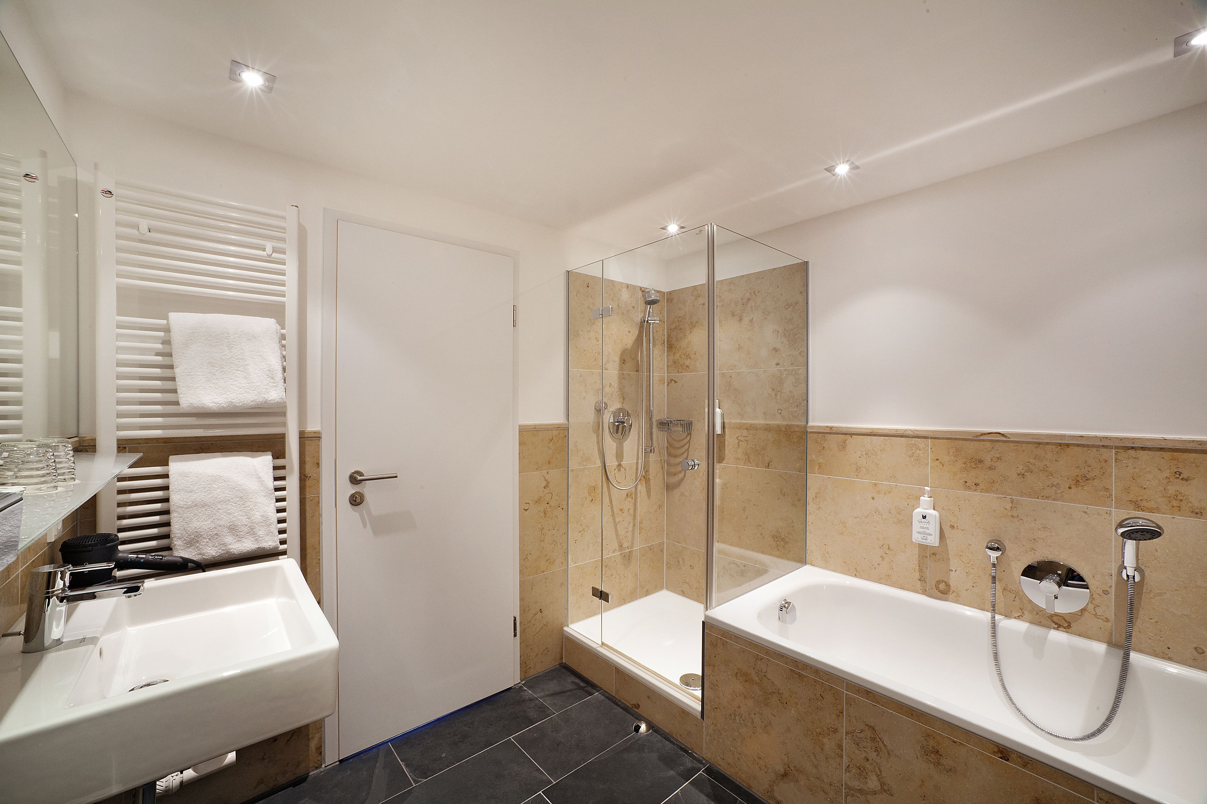 A modern bathroom with a glass-enclosed shower, a separate bathtub, and a vanity with a sink and towel rack.