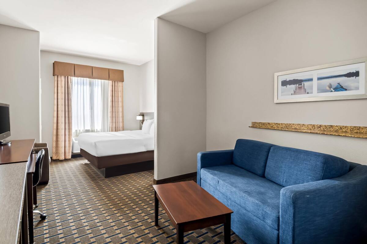 Ein Hotelzimmer mit einem Bett, einem blauen Sofa, einem Holztisch, einem Schreibtisch mit Stuhl und einem Fernseher.