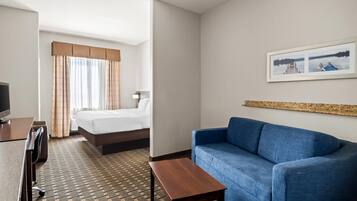 Ett hotellrum med en säng, en blå soffa, ett träbord, ett skrivbord med en stol och en tv.