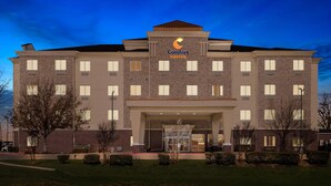 Un hôtel à plusieurs étages, reconnaissable à son grand panneau « Comfort Suites », à son entrée bien éclairée et à son parterre aménagé.