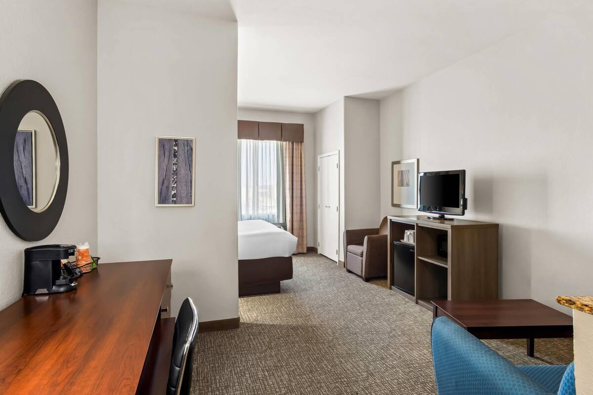Ein Hotelzimmer mit einem Holztisch, einem Fernseher, einem Bett und einer Sitzecke mit einem blauen Sessel.