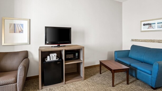 Habitación de hotel con un sofá azul, una pequeña mesa de madera, un televisor sobre un mueble de madera, un refrigerador y un microondas.