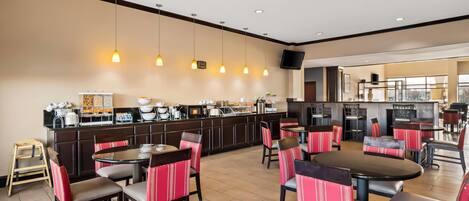 Un restaurante con mesas redondas y sillas tapizadas de rojo, una barra con equipo de cocina y un televisor montado en la pared.