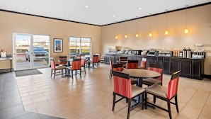Un vaste espace intérieur comprenant plusieurs tables et chaises, un coin cuisine avec un bar, et de grandes fenêtres offrant une vue sur l’extérieur.