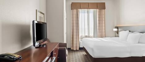Habitación de hotel con una cama, un escritorio con televisor, teléfono y ventana con cortinas.