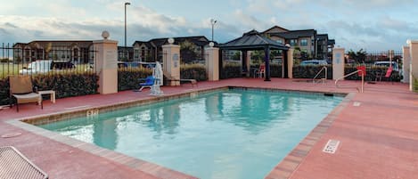 A rectangular pool with a tiled edge, surrounded by a red surface, and a gazebo in the background.
