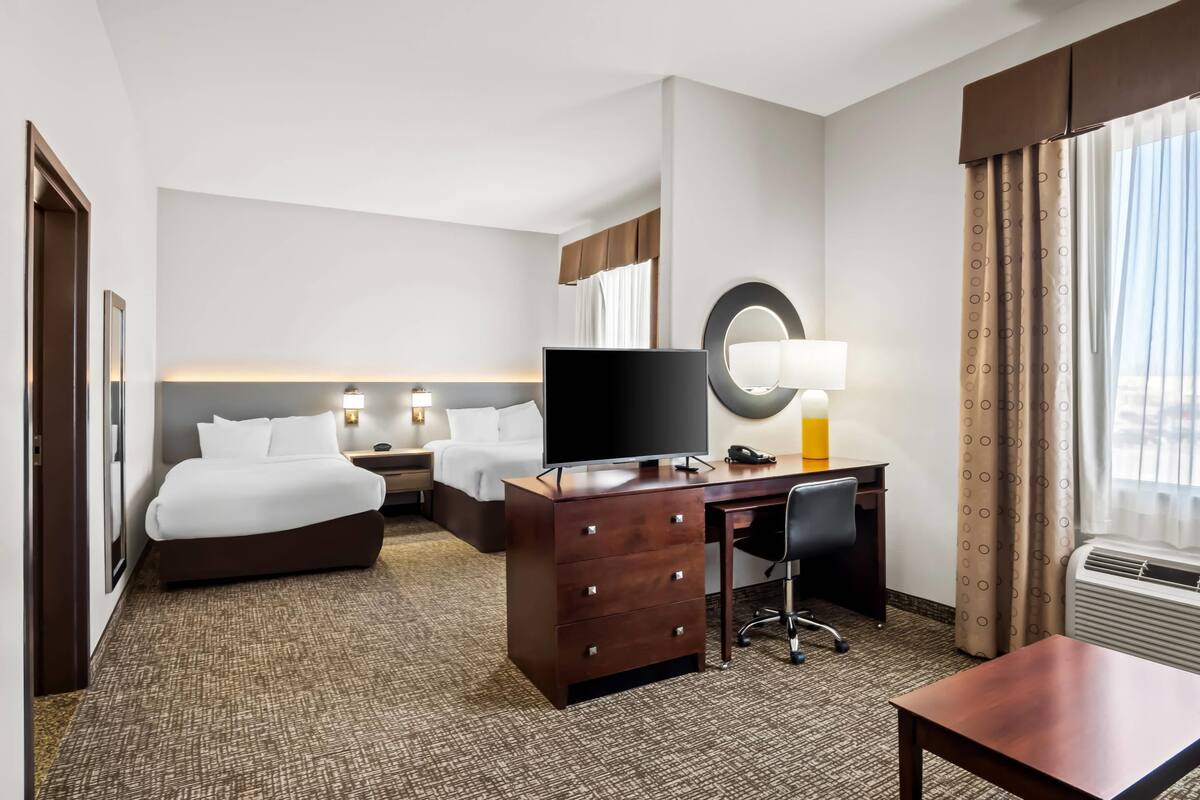 Ein Hotelzimmer mit Bett, Schreibtisch mit Computer, Stuhl, Kommode, Fernseher und Lampe.