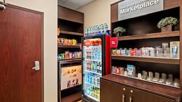 Habitación de hotel con minibar, nevera llena de bebidas y estantes con aperitivos y artículos de aseo.