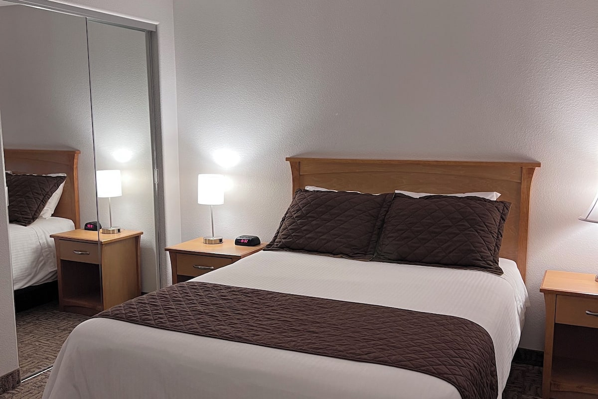 Ein Hotelzimmer mit einem großen Bett, zwei Nachttischen, einem Spiegel und einem Teppichboden.