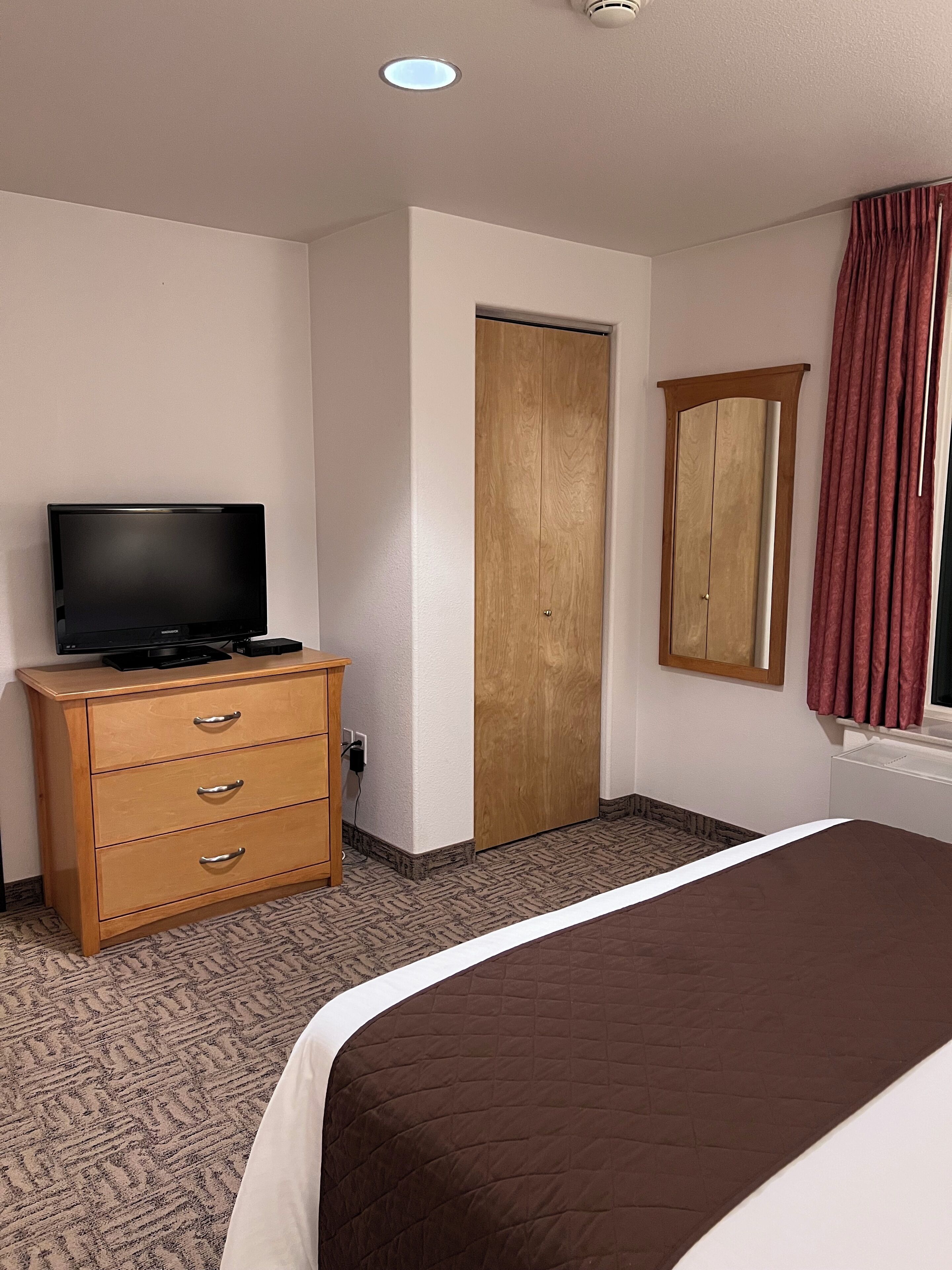 Una habitación de hotel con una cama, un aparador de madera, un televisor, un armario y un espejo.