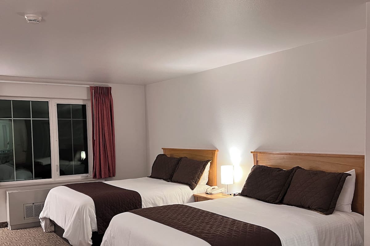 Ein Hotelzimmer mit zwei Betten, einem Fenster mit Vorhängen, einer Nachttischlampe und einem Thermostat.