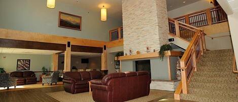 A spacious living area with leather sofas, a stone fireplace, and a wooden staircase.