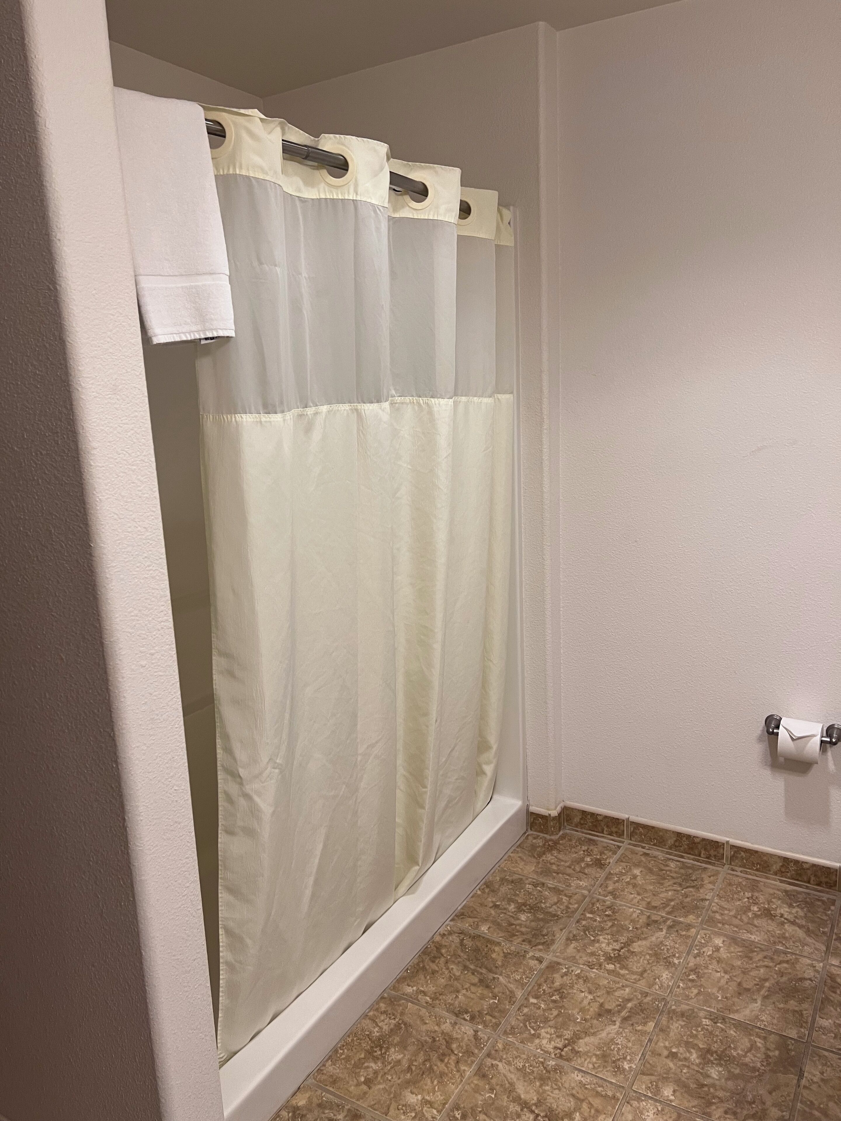 A bathroom with a shower curtain, a toilet paper holder, and a tiled floor.