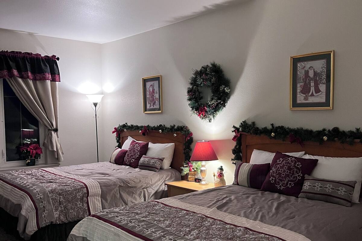 Ein Hotelzimmer mit zwei Betten, einem Nachttisch mit Lampe, einem an der Wand befestigten Kranz und einem gerahmten Bild.